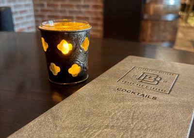 Burdock + Bitters cocktail menu on table next to lit decorative candle